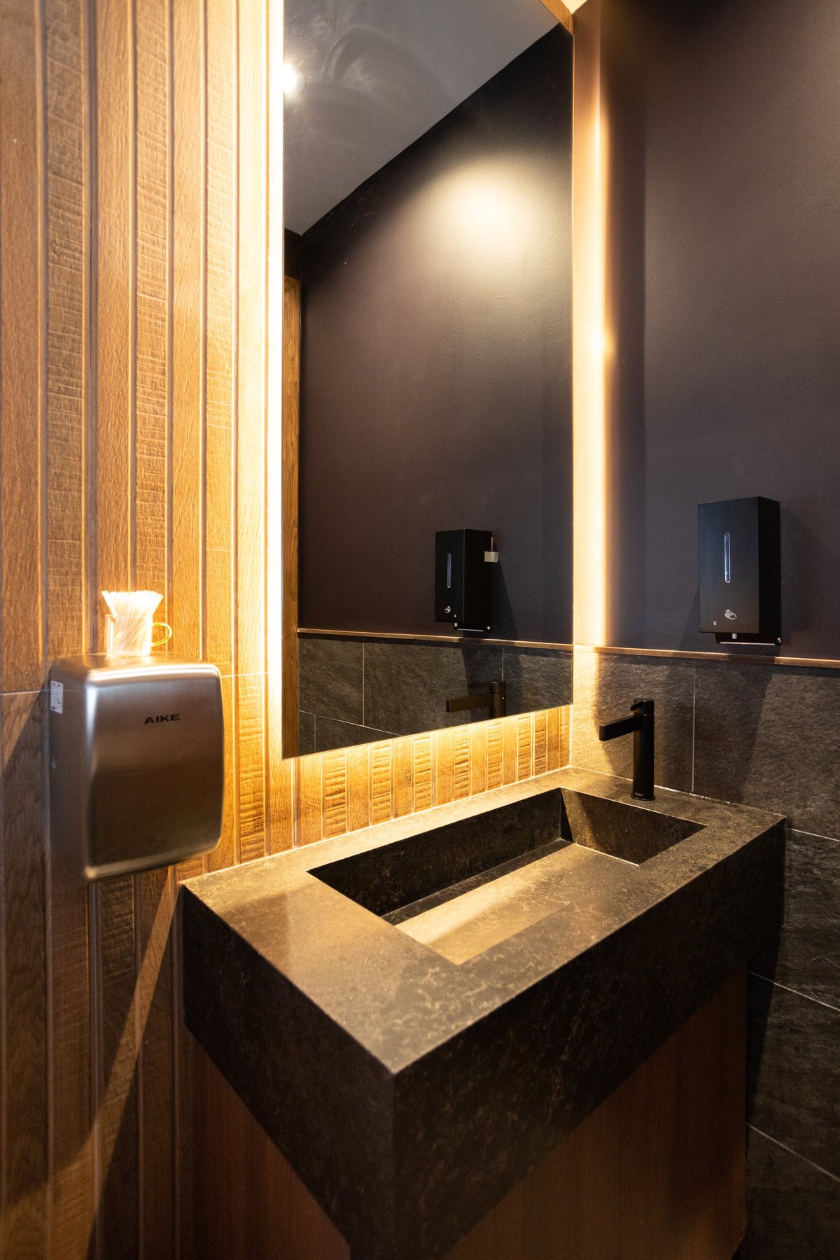 Modern bathroom with dark stone sink, illuminated mirror with LED lighting, and wood-textured walls