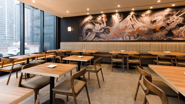 Modern restaurant interior with wooden tables, mid-century chairs, large dragon artwork, and floor-to-ceiling windows overlooking city skyline