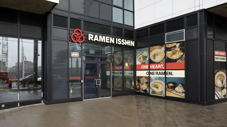Ramen Isshin restaurant storefront with black facade, glass doors, red logo, and menu displays showing noodle dishes