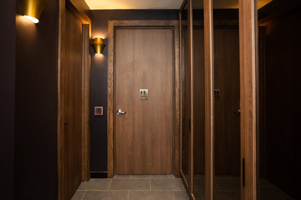 Modern elevator hallway with dark wood paneling, warm lighting, and tile flooring leading to closed doors