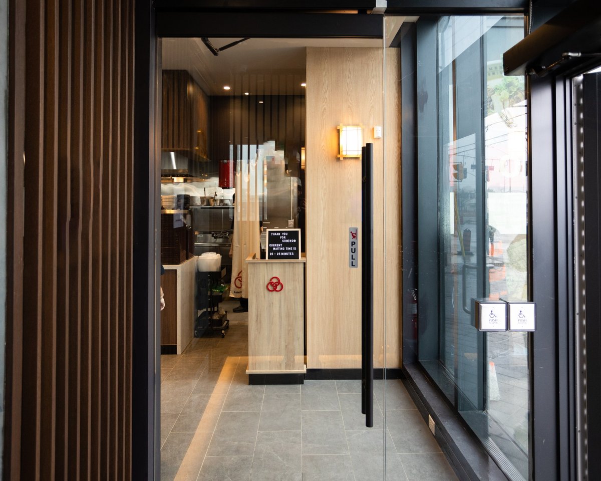 Modern restaurant or café entrance with wooden slat door, glass storefront, and minimalist interior visible through the entry